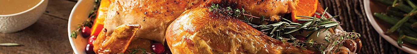 Roasted turkey on a platter with herbs, orange slices, and cranberries.